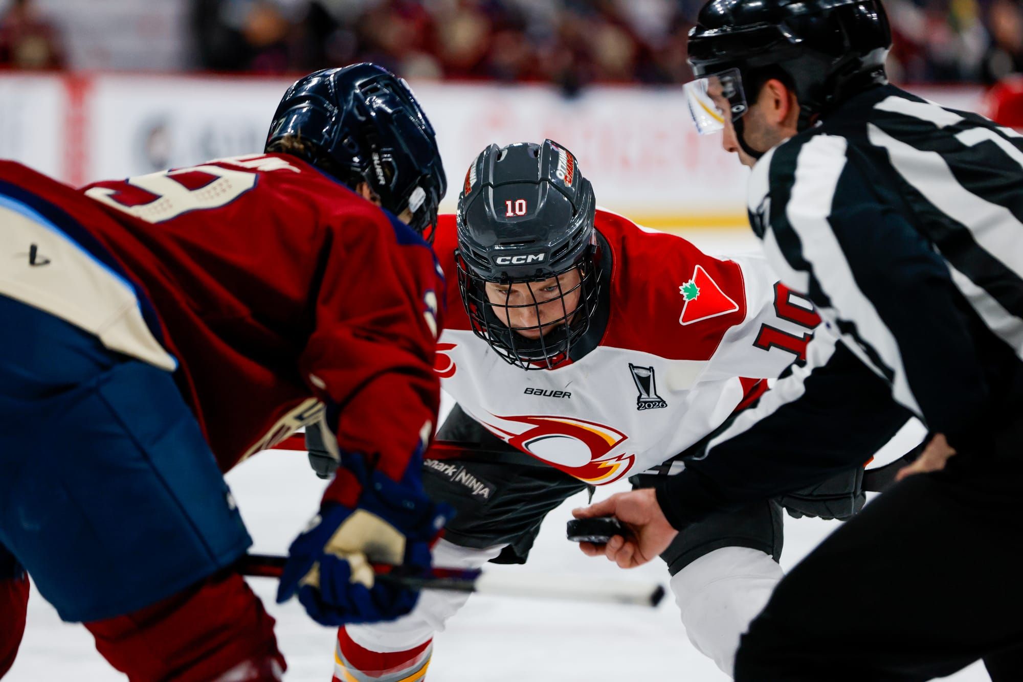 Ottawa Charge forward Alexa Vasko prepares to take a face-off against Montreal Victoire forward Marie-Philip Poulin, as an official holds a puck between the players.