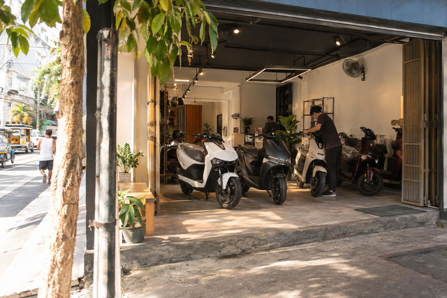 Illustrative unbranded electric-motorcycle dealer storefront on a tropical city street