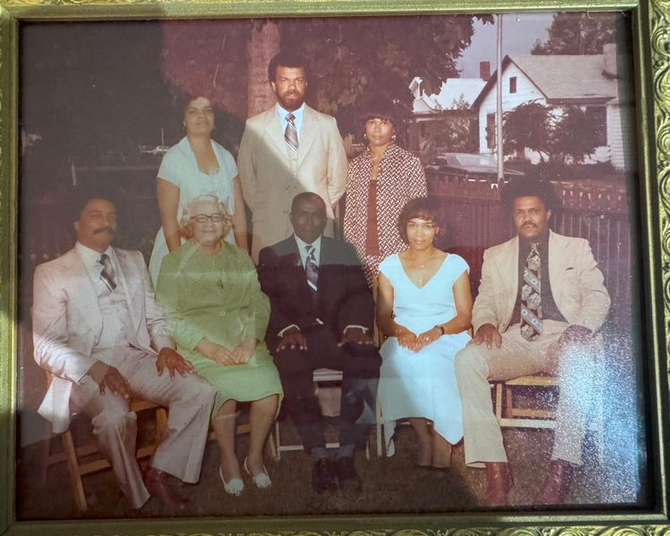Eight African-Americans sitting in two rows for a formal family picture in their Sunday best.  Three are standing, five are sitting.