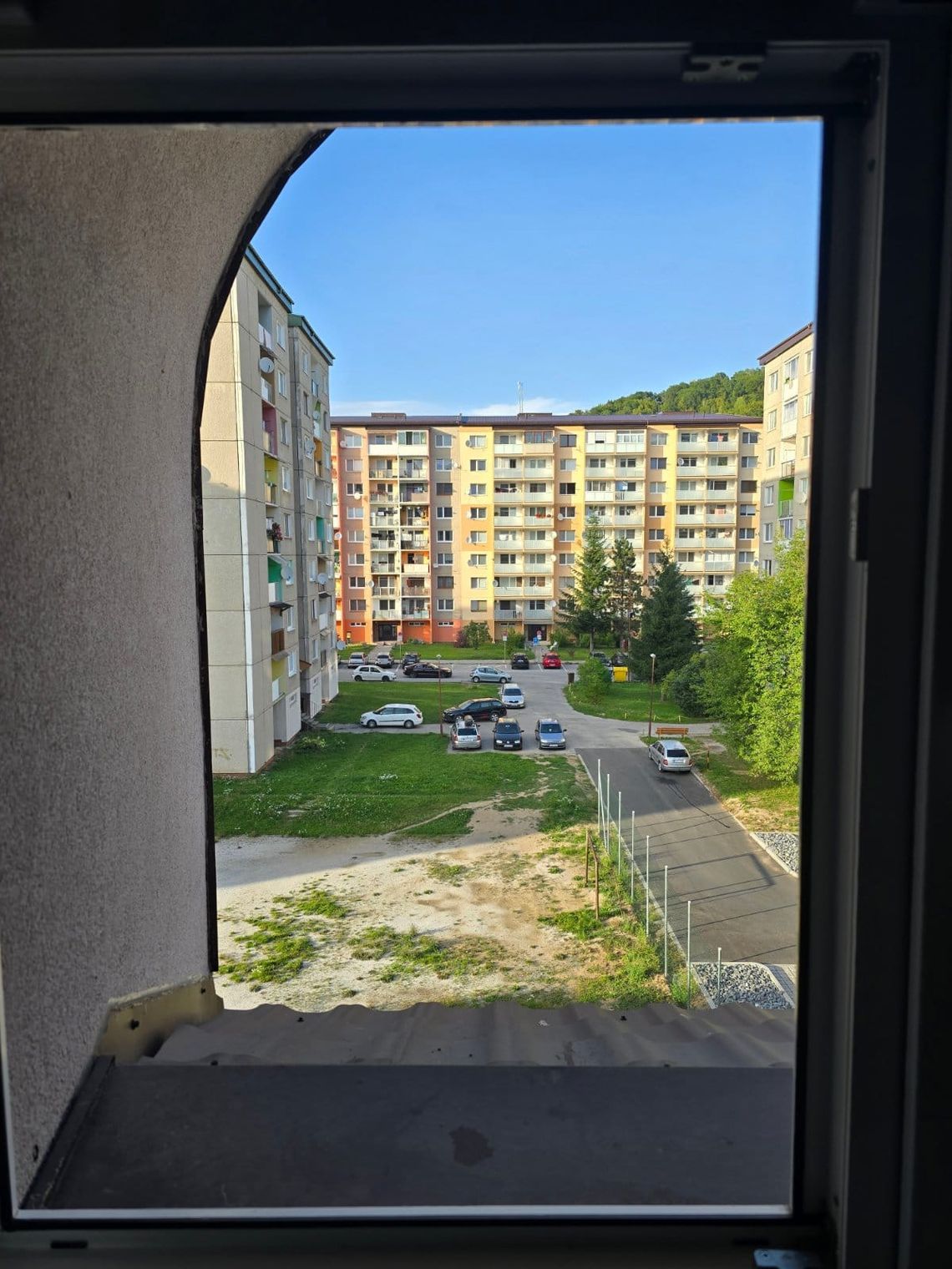 View from window of courtyard with patchy grass, parked cars and apartment blocks. 
