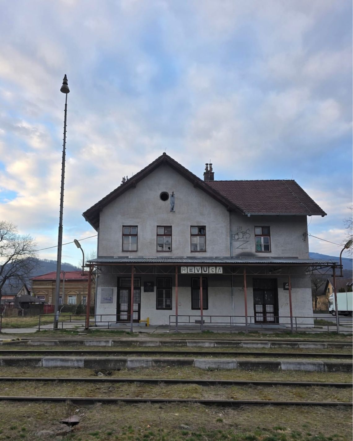 Old building with train tracks in foreground and mountains in background. 