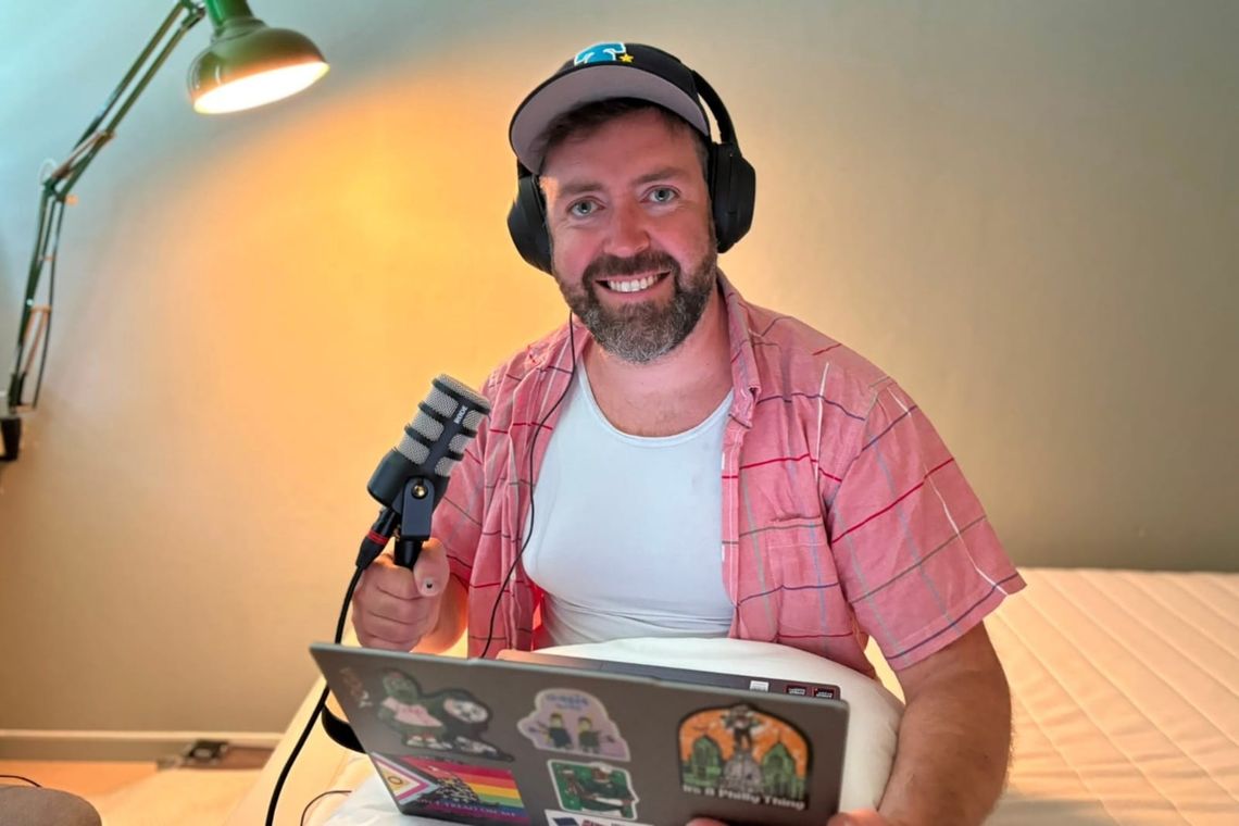 Man wearing big headphones with mic near face and computer in lap with lamp illuminating the scene.