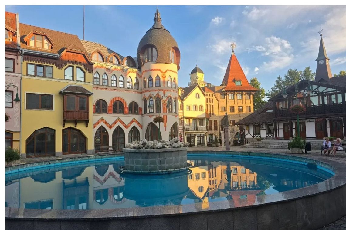 Colorful buildings under blue sky and with pool in foreground reflecting the buildings. 