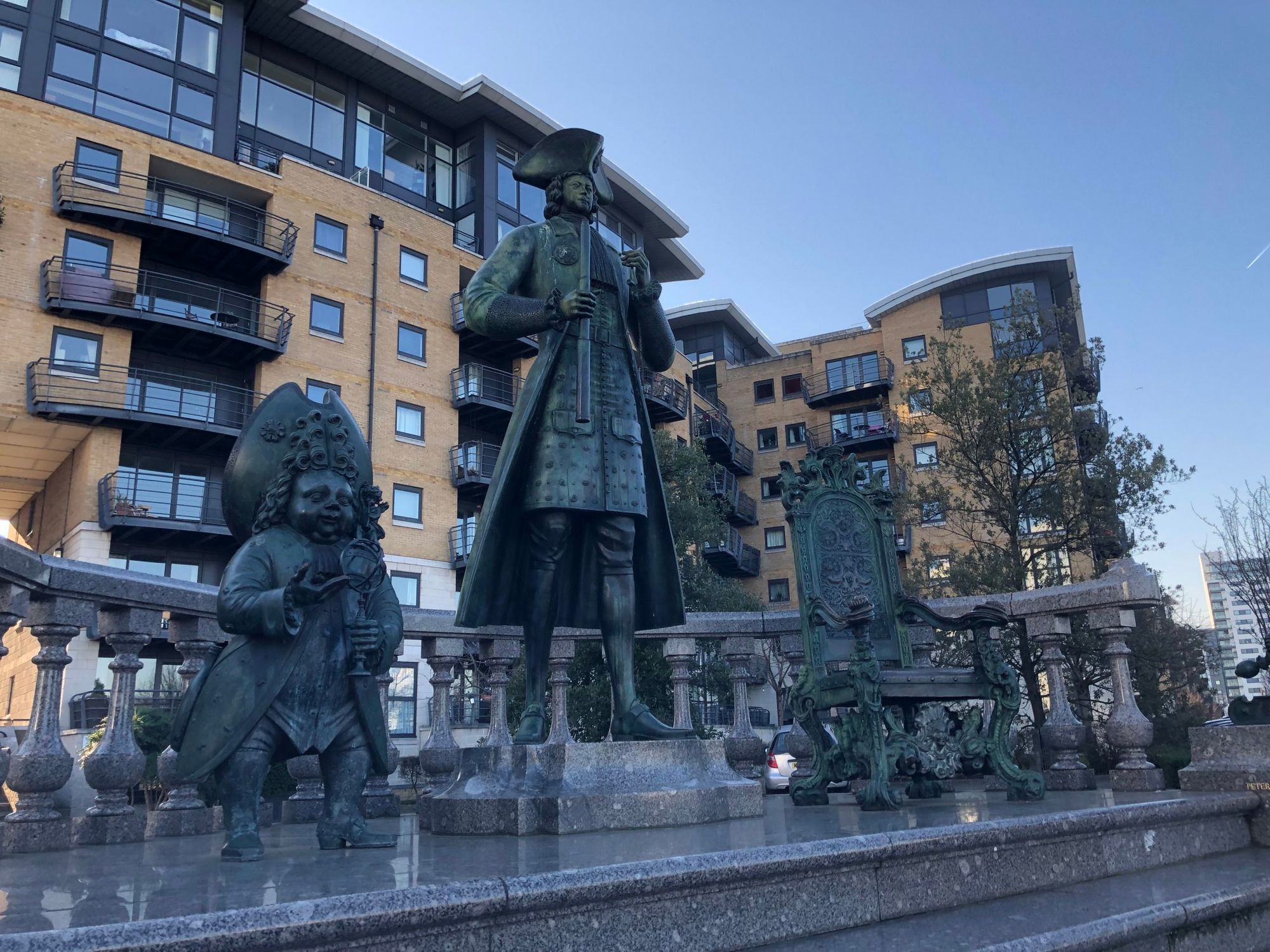 Statue of Peter The Great standing on a plinth. To the left is a statue of a court dwarf and to the right is a statue of a th