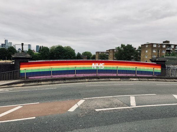 Rainbow painting with word NHS in white over it on wall of Blackhorse Bridge by the pavement and road