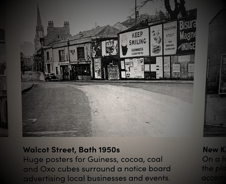 Underneath a description: Huge posters for Guiness, cocoa, coal and Oxo cubes surround notice board advertising local businesses and events