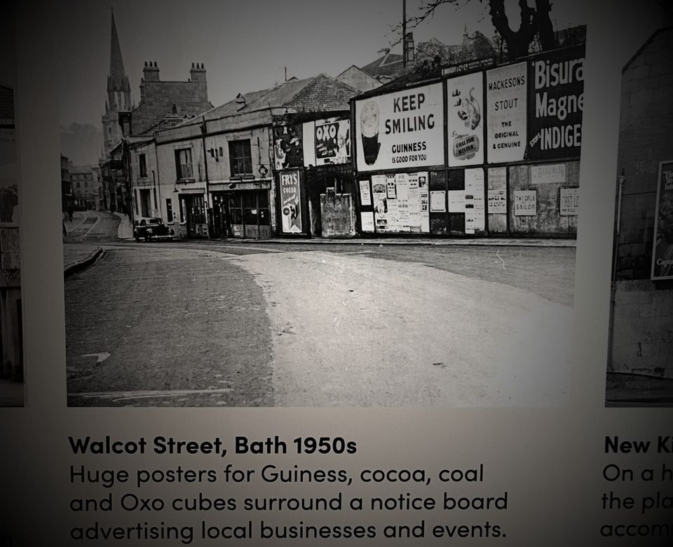 Underneath a description: Huge posters for Guiness, cocoa, coal and Oxo cubes surround notice board advertising local businesses and events