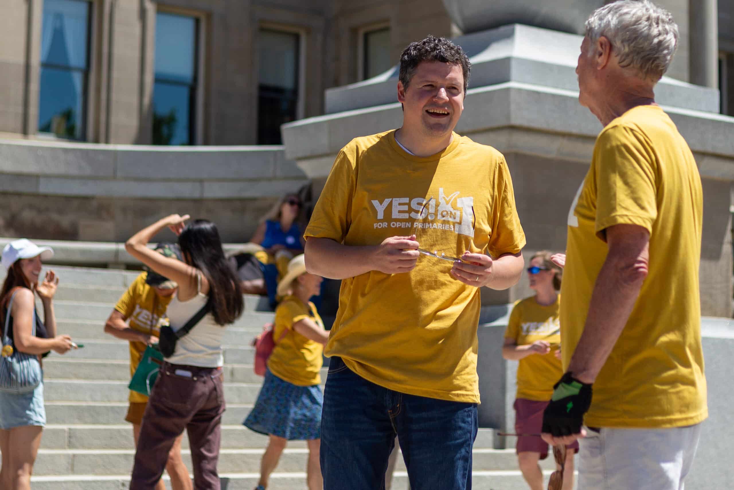 Luke Mayville, co-founder Reclaim Idaho that is part of the Idahoans for Open Primaries coalition, talks with an initiative supporter after supporters submitted signatures for final review for the ballot initiative. Both are wearing yellow shirts that say "Yes! on 1 for open primaries"