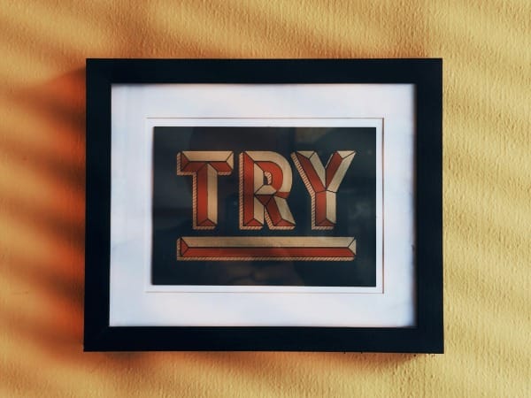 Framed try sign on a textured yellow wall with shadows