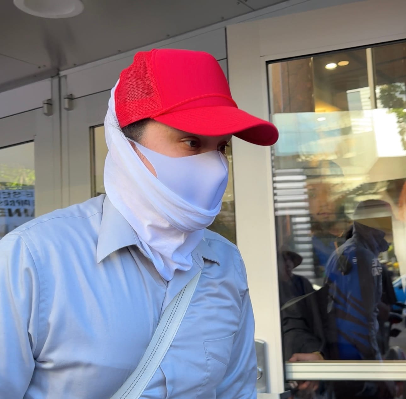 Neo Nazi wearing a pale blue button up, white neck gator and face mask, and red baseball cap