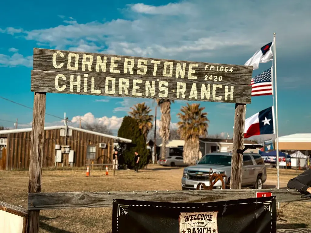 Sign at the ranch that says "cornerstone Childrens Ranch" with multiple flags in the background