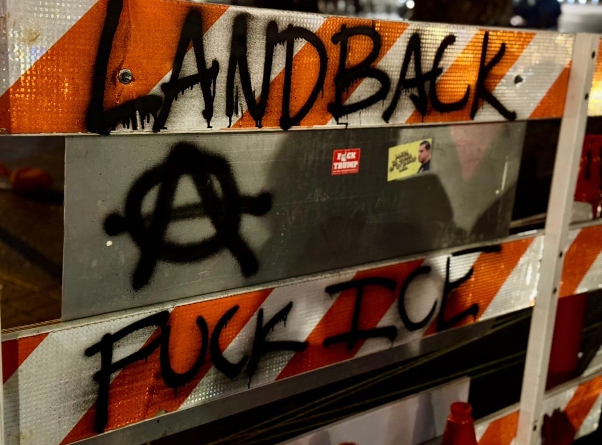 Barricade at the permanent vigil, says “land back” and “fuck ICE” with a circle A 