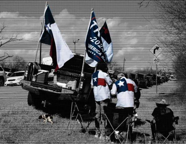 a black and white photo (with reds and blues visible) of people at the rally having a BBQ near their truck which has multiple flags including a Trump and Christian nationalist one.. 