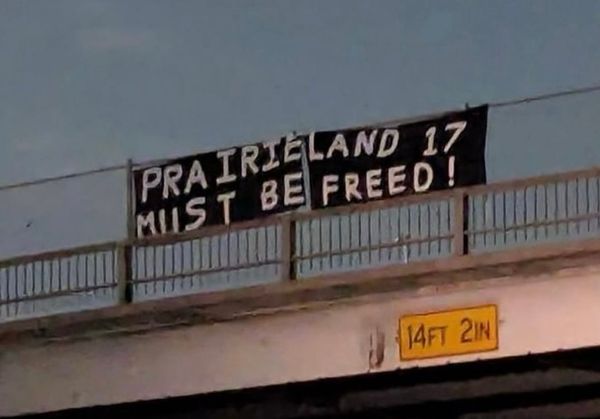 Banner drop in solidarity with the Prairieland defendants. Banner is black with white writing and says “Prairieland 17 must be freed!"