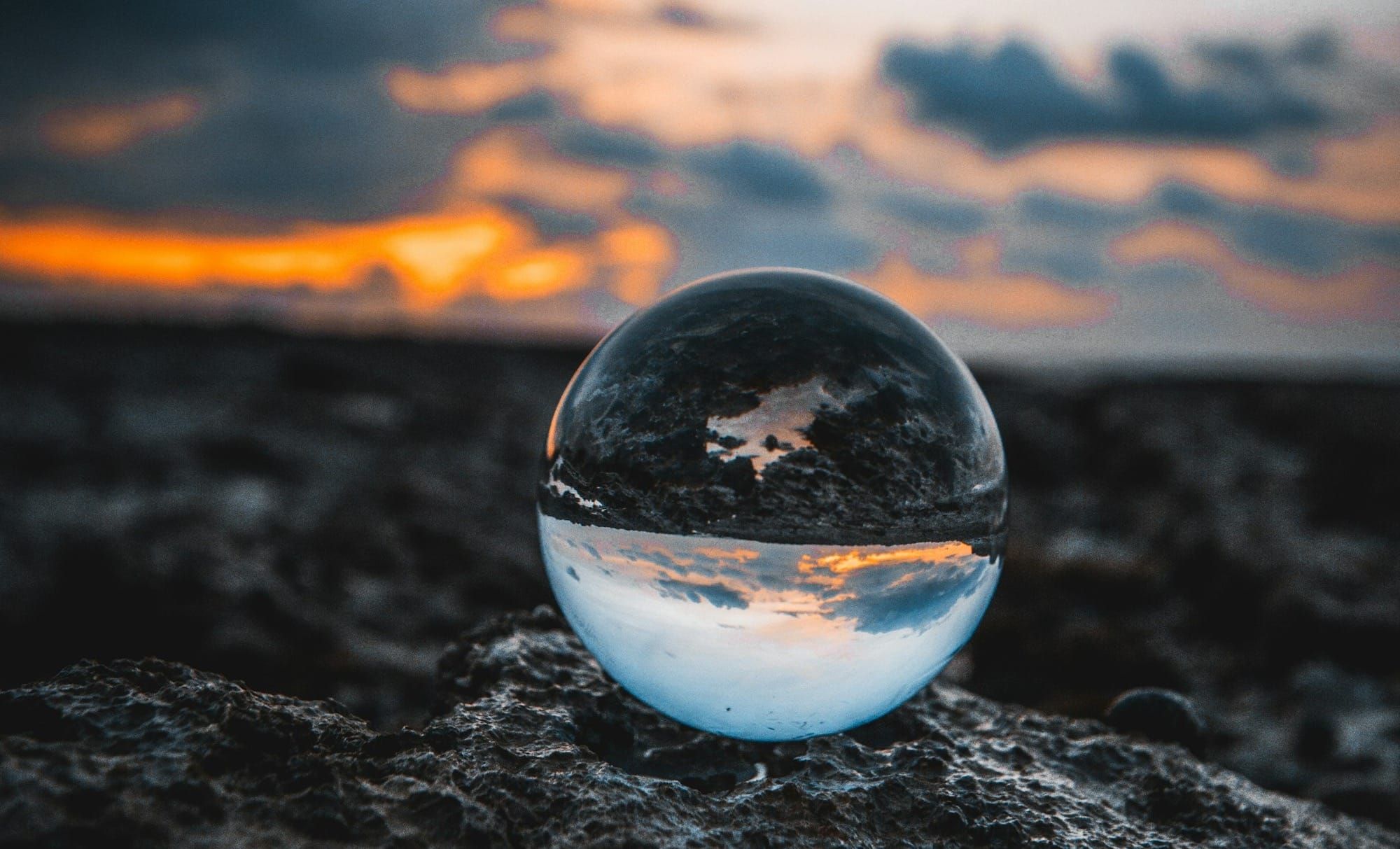 a clear crystal globe with a sunset behind, the sky and land are inverted in their reflection within