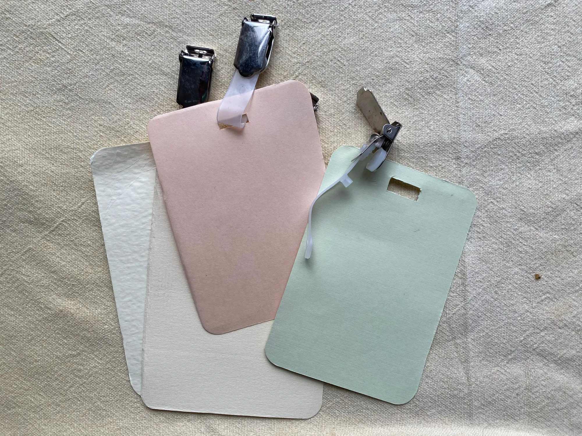 Four rectangular pieces of card on a tablecloth. Each has a hole at the top where a plastic clip is inserted.