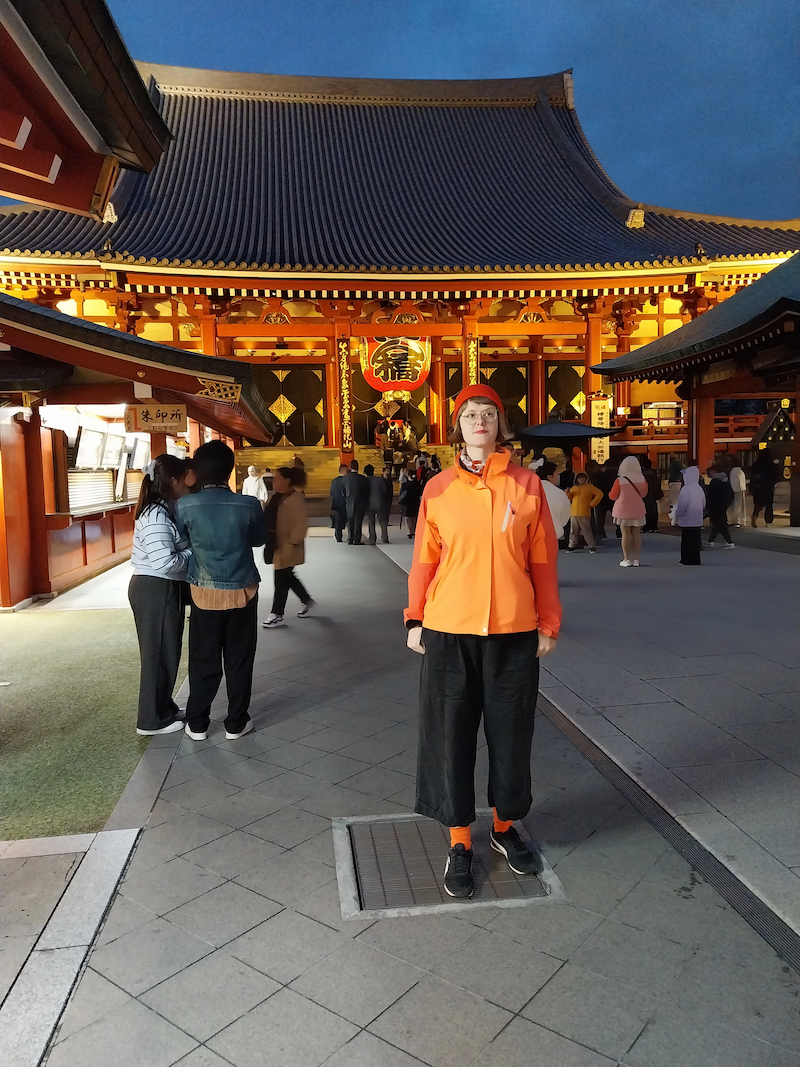 Me wearing an orange raincoat and socks, with black trousers and trainers, standing in front of Sensō-ji, Tokyo's oldest temple.