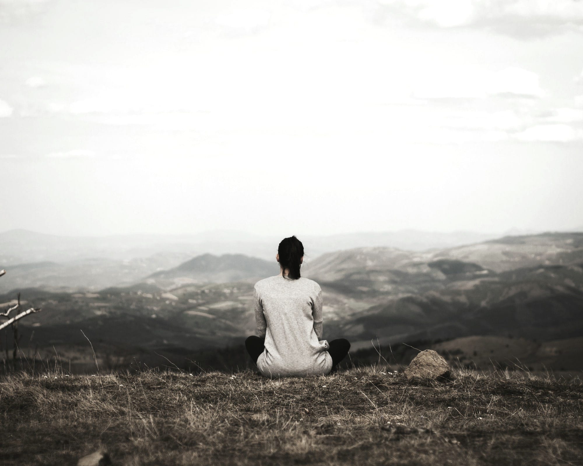 woman sitting on cliff overlooking mountains during daytime