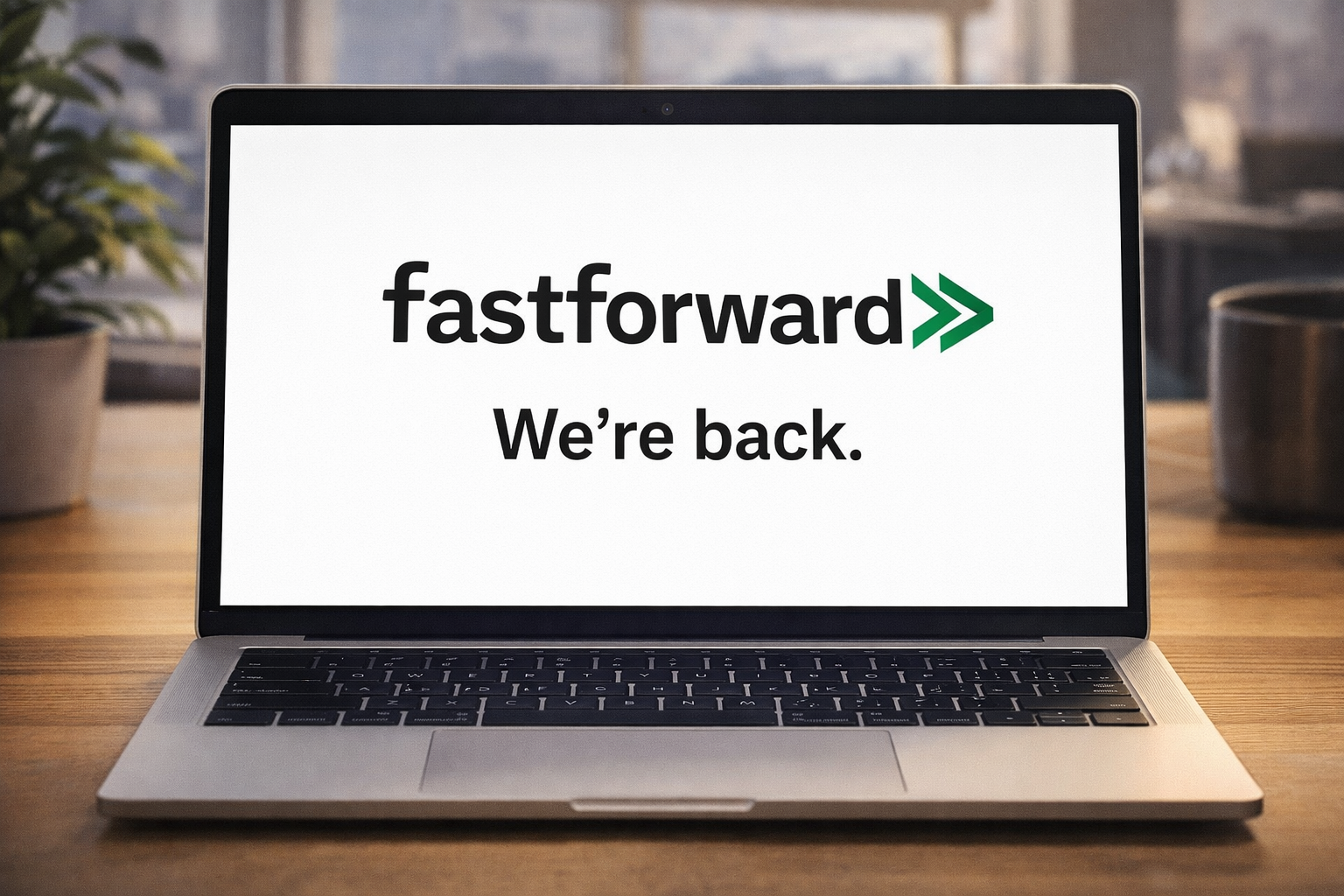 Open laptop on a desk displaying the FastForward logo and the words “We’re back.” on a white screen, with a softly blurred office background behind it.