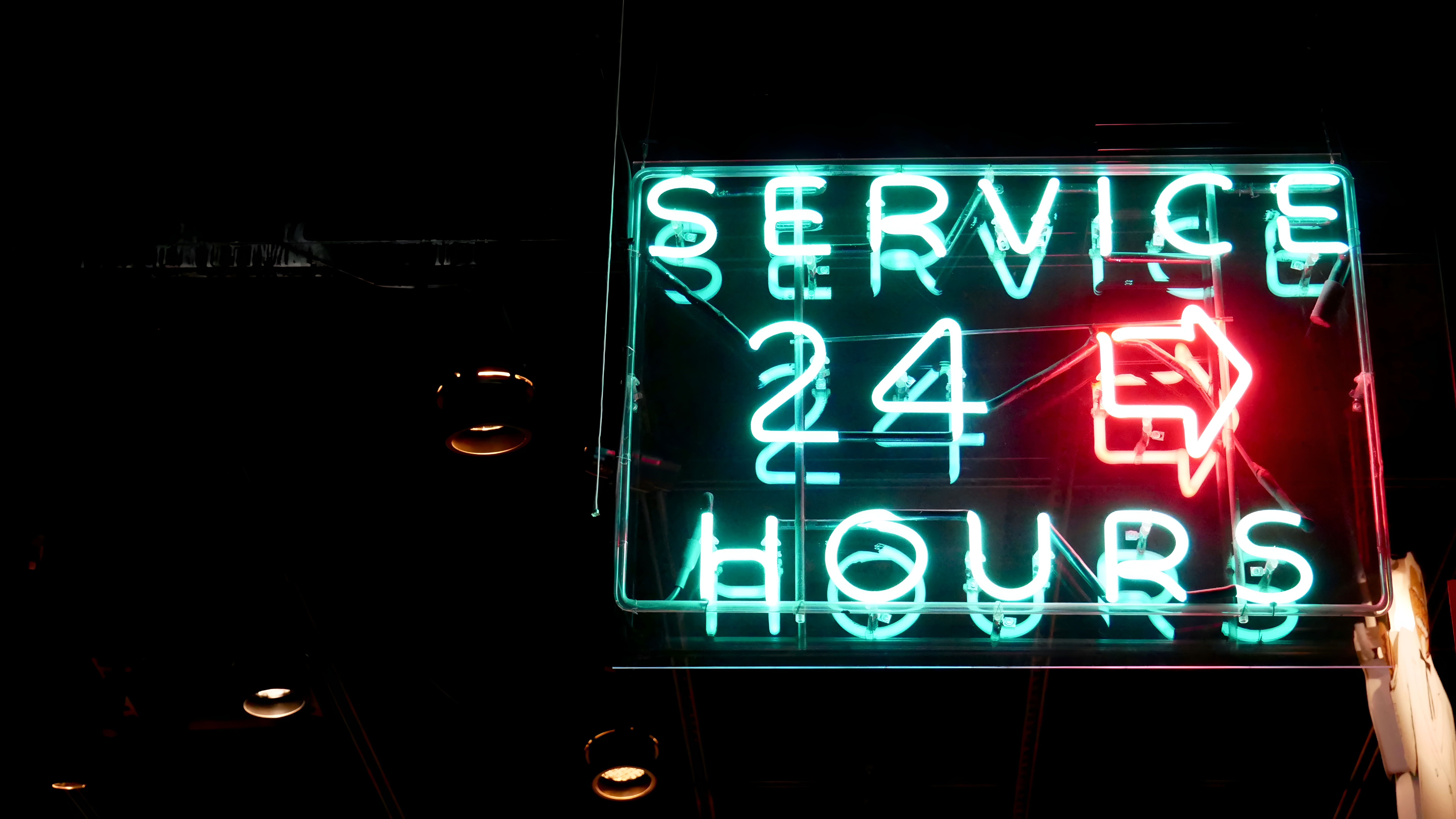 Neon sign glowing against a dark background that reads "SERVICE 24 HOURS" with a red arrow pointing right.