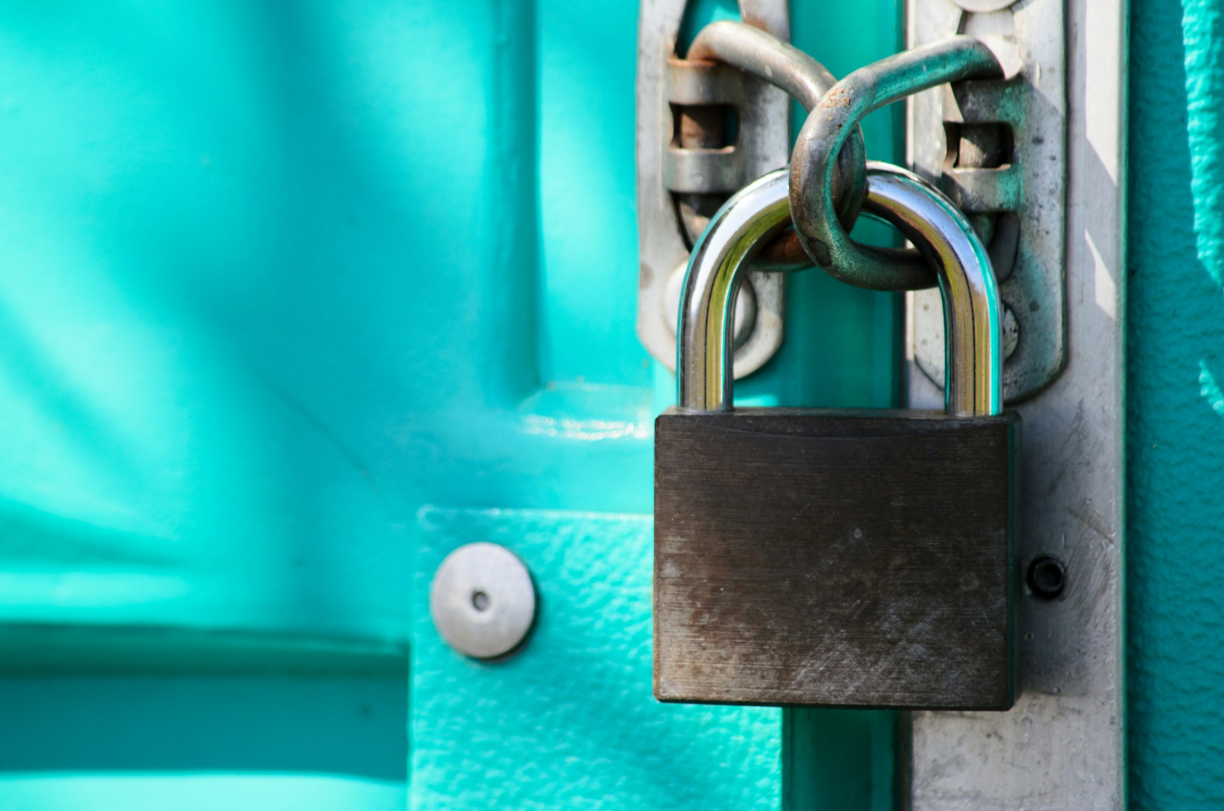 Brass padlock on bright teal door.