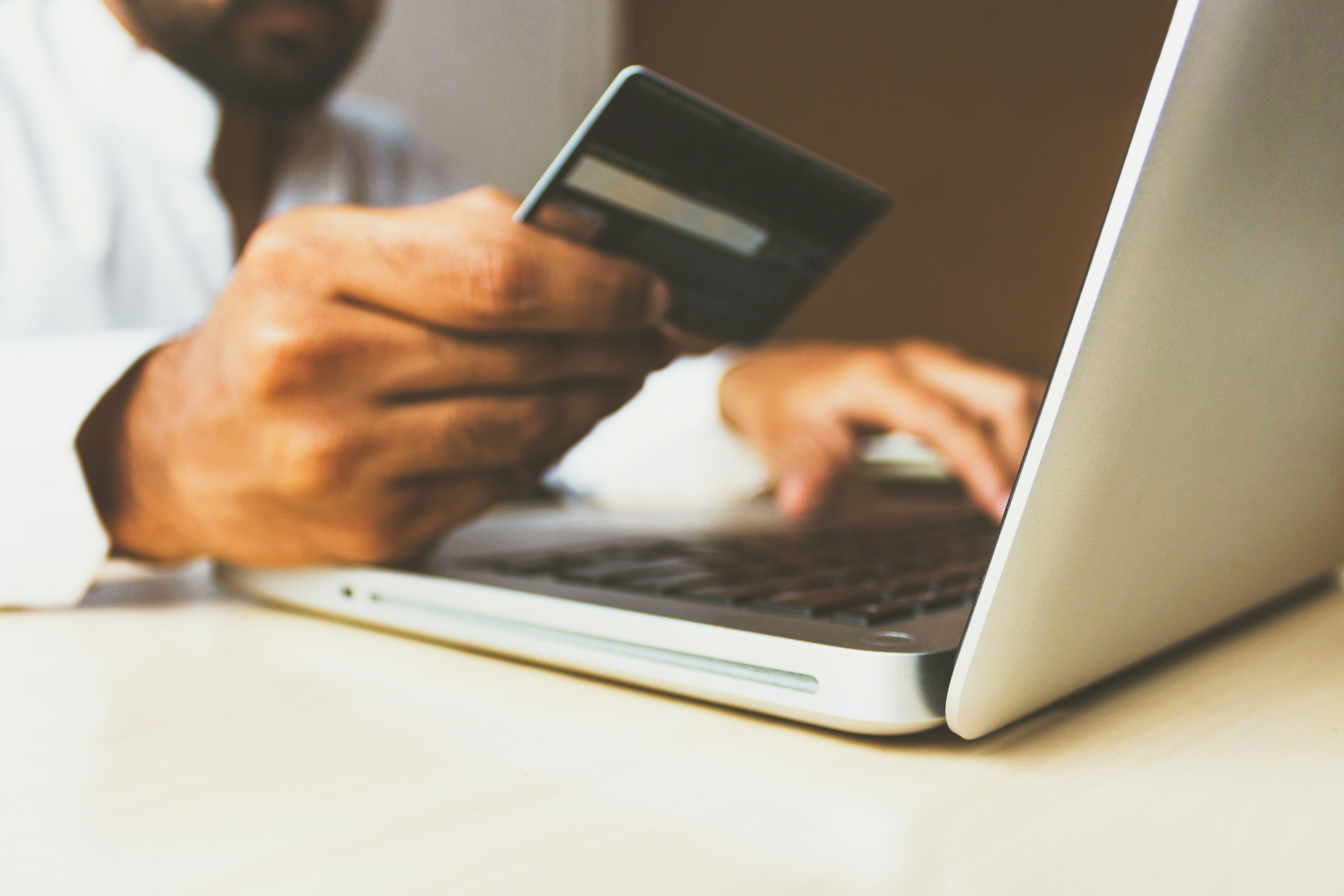 Man holding a credit card while typing the number into his laptop.