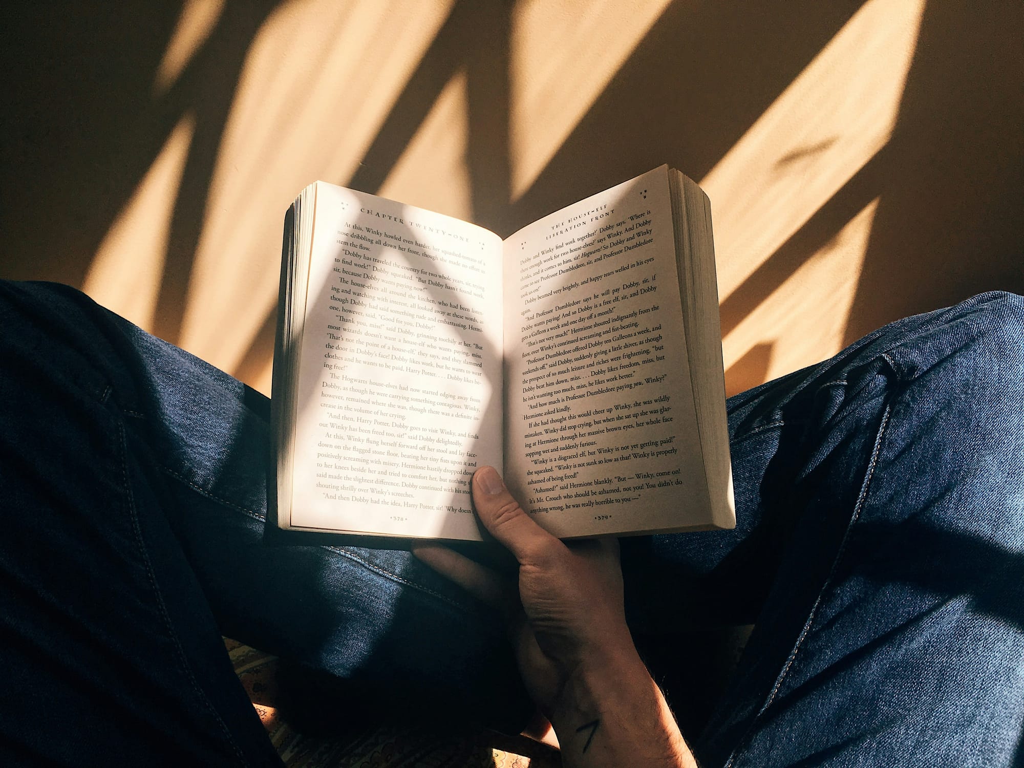 Person sitting cross-legged reading an open book in warm sunlight.
