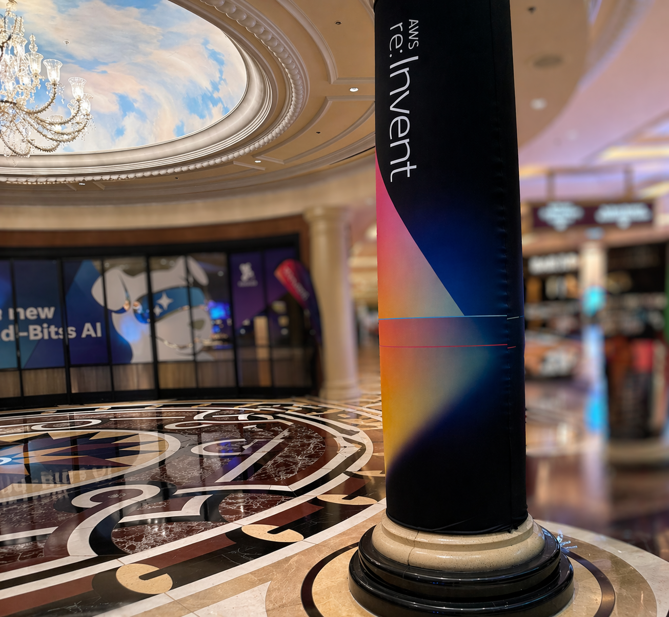 AWS re:Invent banner on a column, with marble floor, chandelier, and painted skylight in focus behind it.
