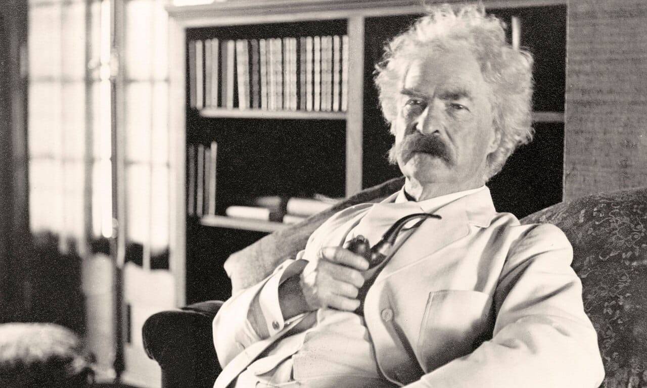 Mark Twain holding a pipe in a white suit in a library.