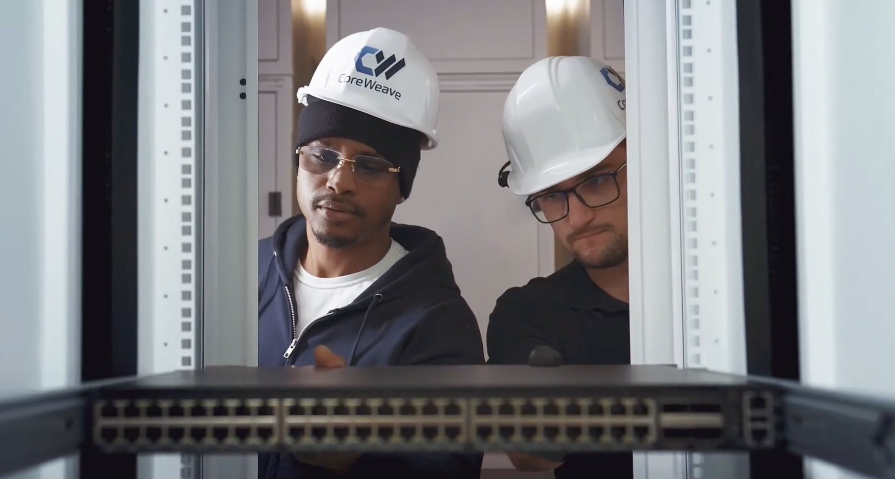 Two men in CoreWeave hard hats building a rack in a data center.