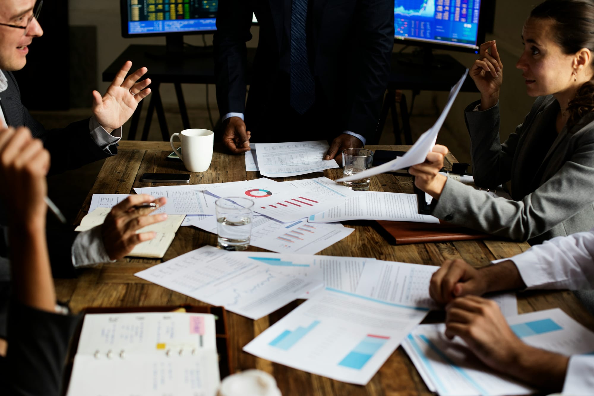Business team debating reports and data spread across a conference table.