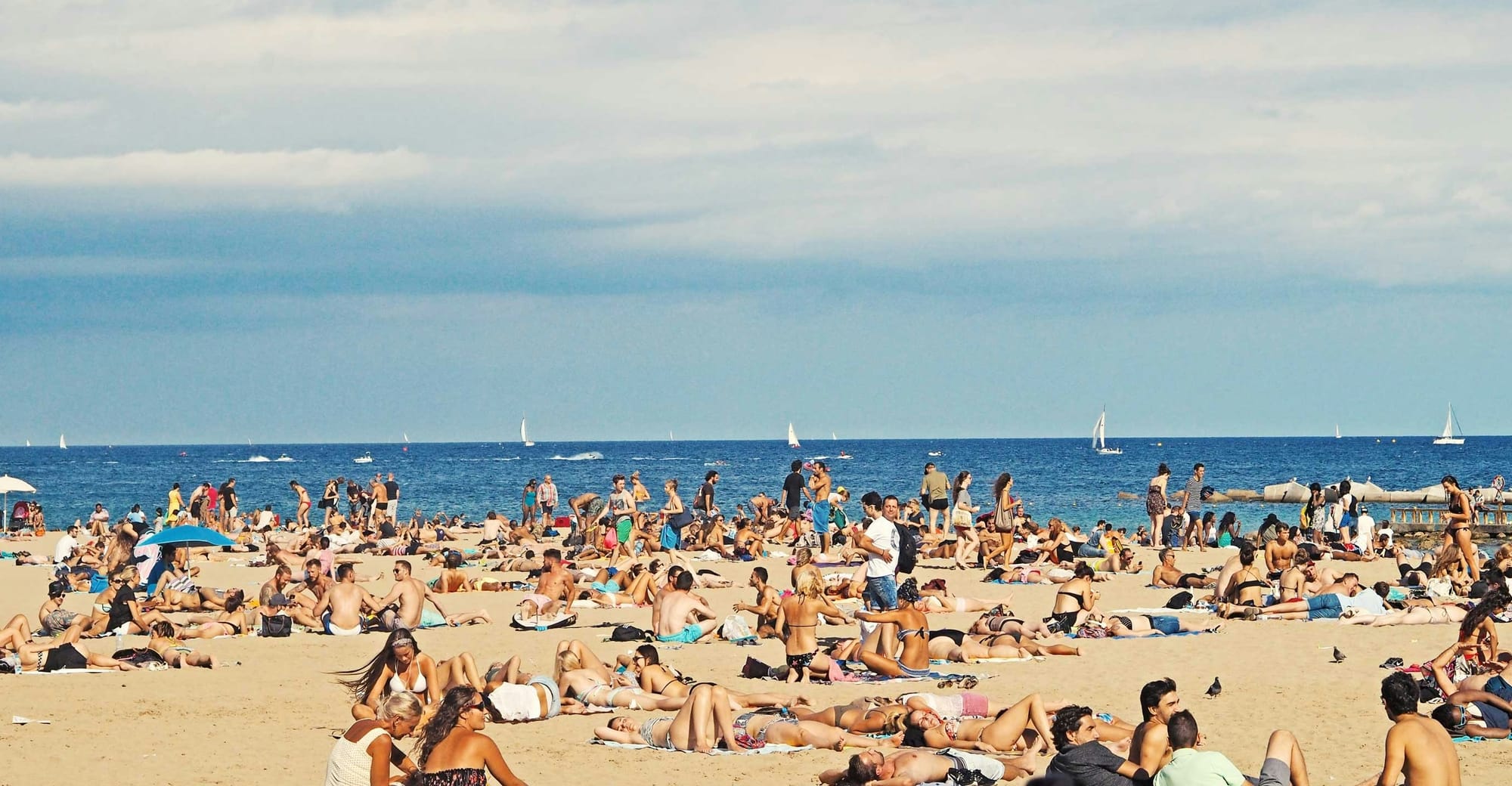 Crowds of people relax and socialize on a busy beach beside the ocean.