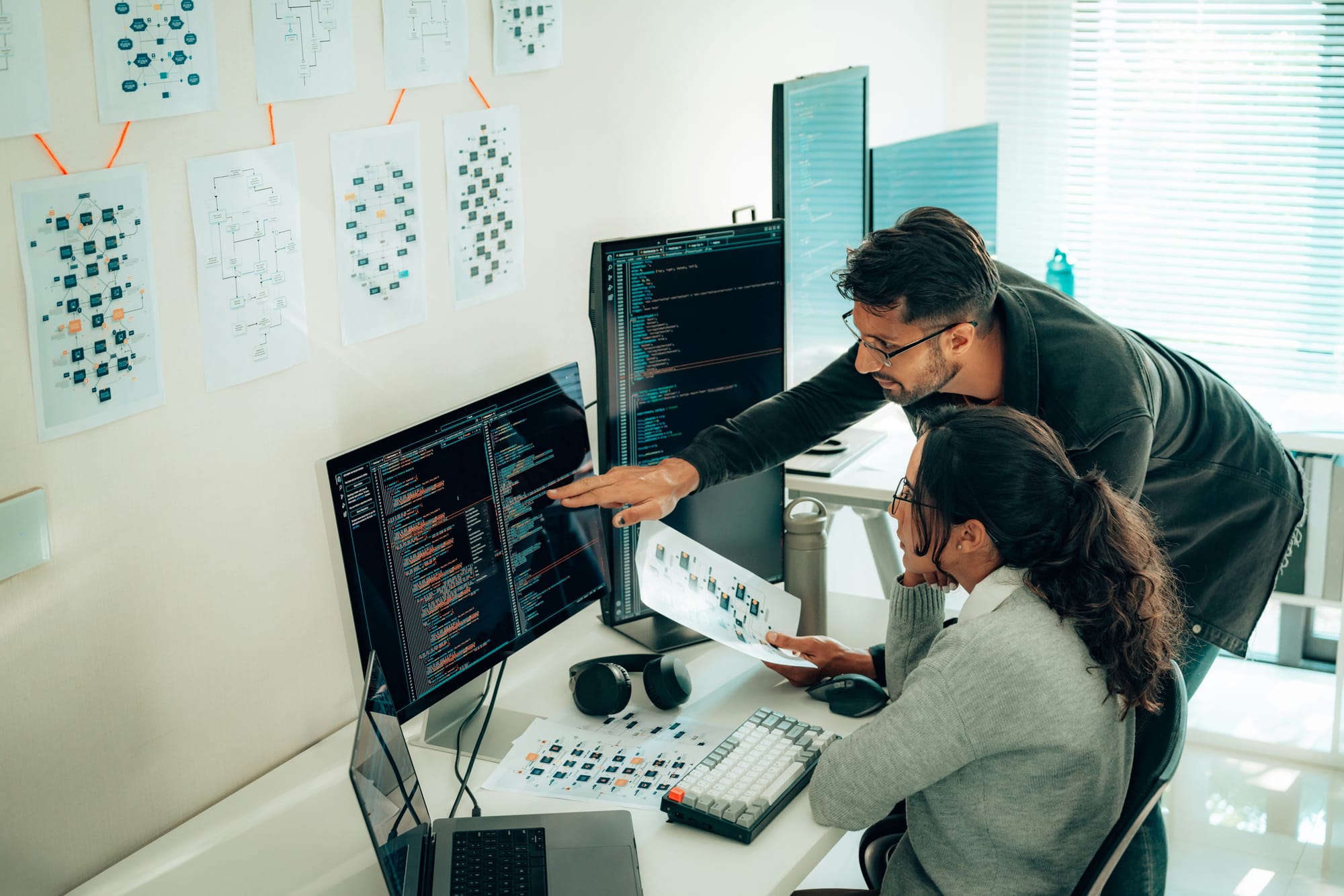 Man and woman working together on code surrounded by technical drawings.