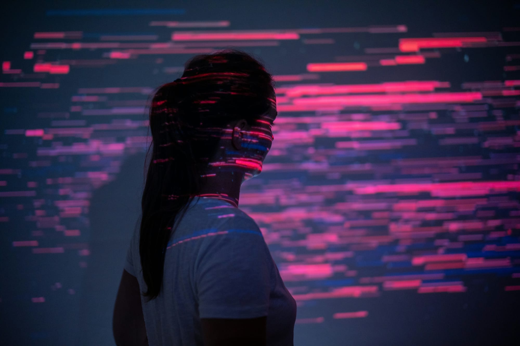 Person standing against a dark background with colorful digital light patterns projected across them.