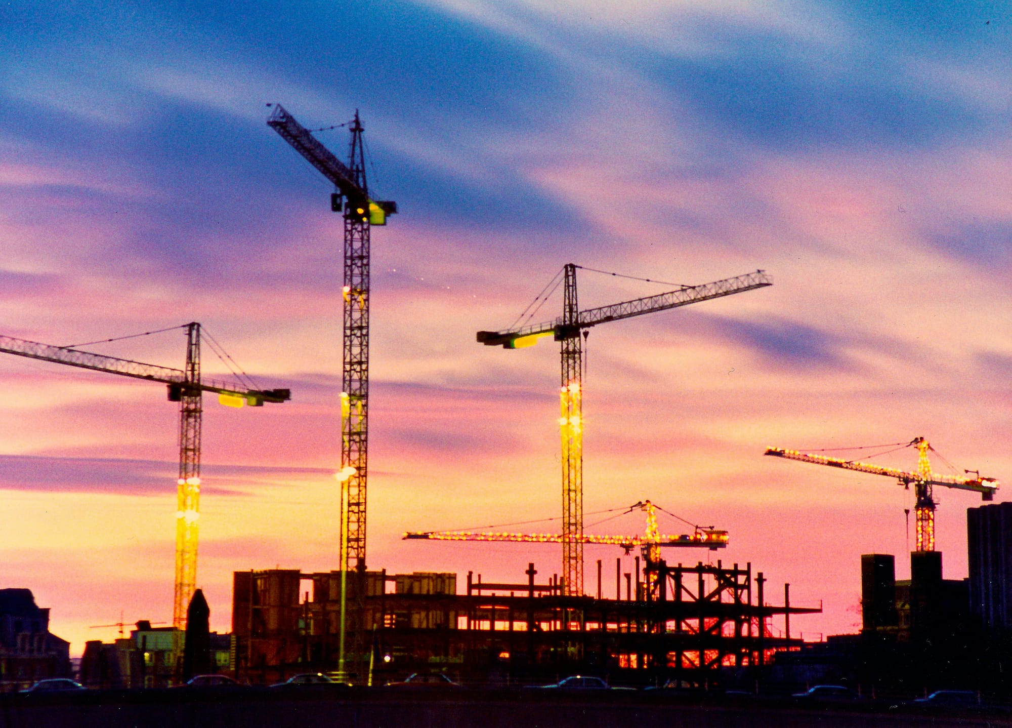 Construction cranes silhouetted against a colorful sunset sky.