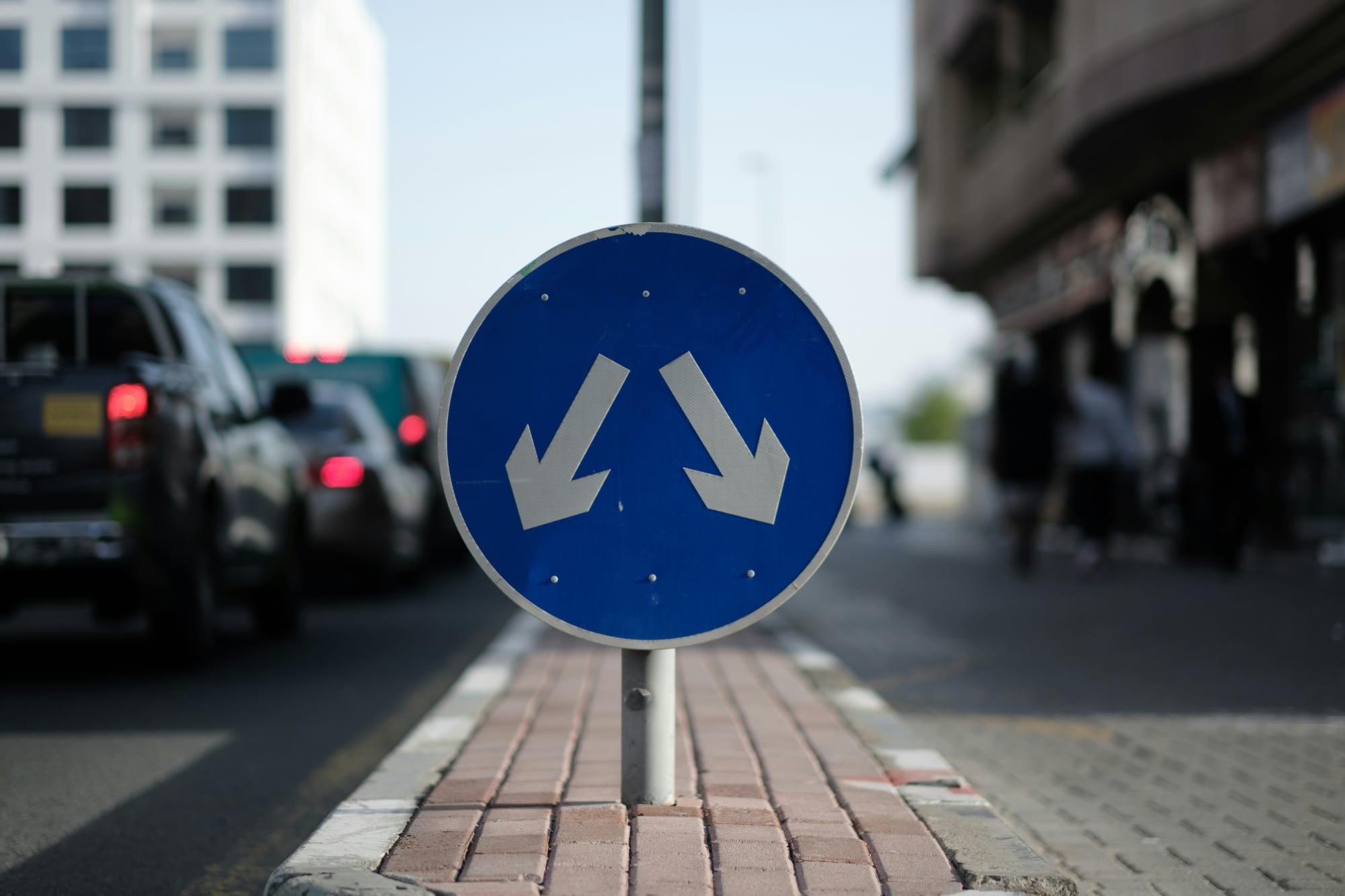 Blue traffic sign with two arrows pointing in opposite directions on a city street.
