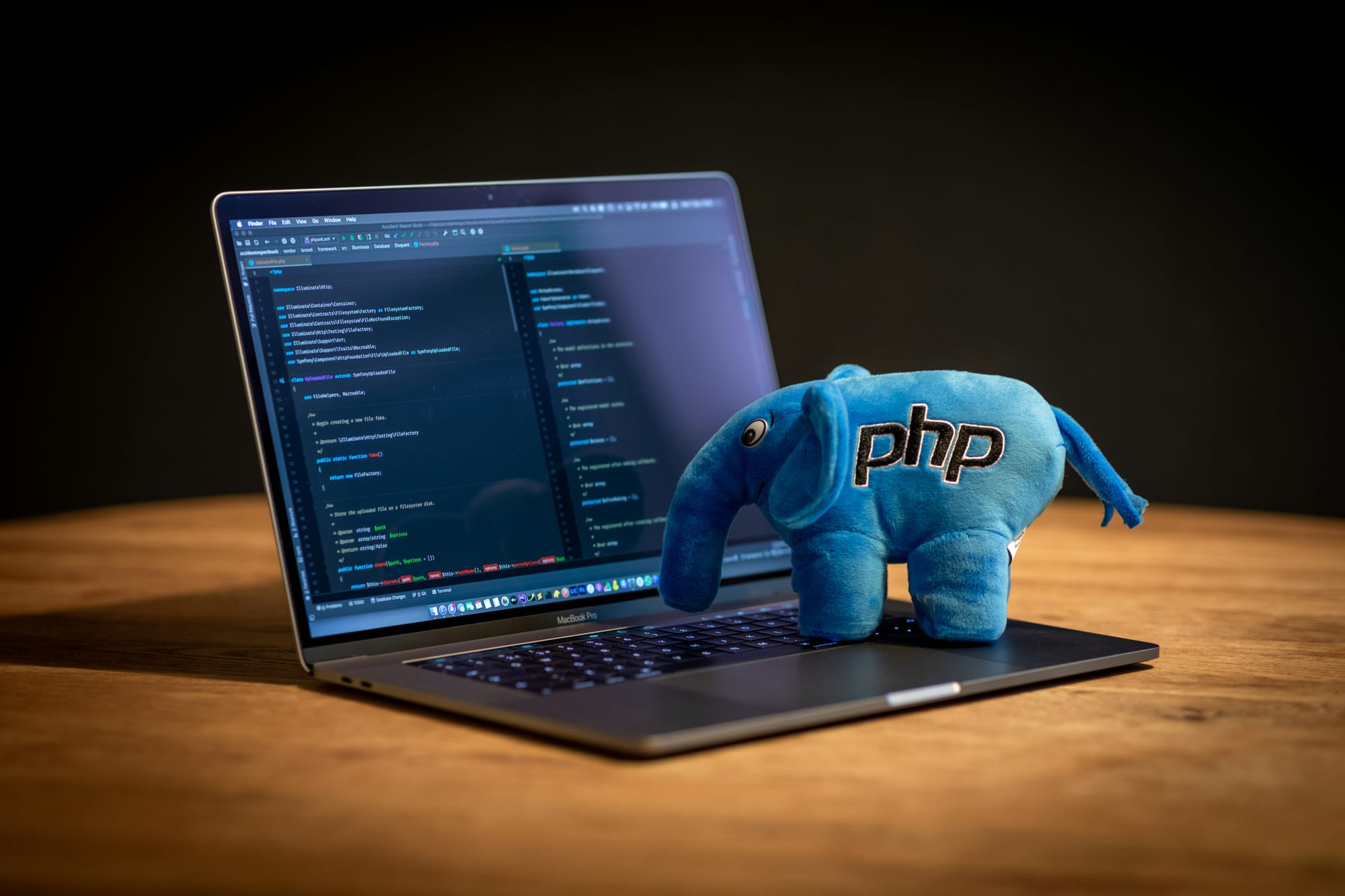 Plushy blue elephant with php on the side standing on laptop with code displayed.