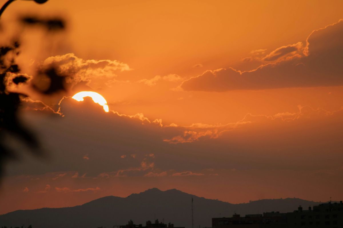 Sunset behind dark clouds with the sun partially hidden, casting an orange glow across the sky and silhouetting mountain ridg