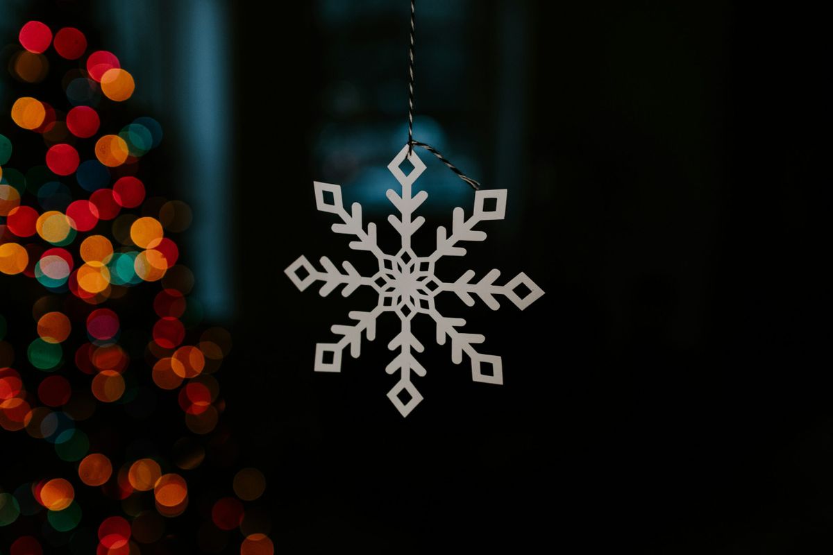 Gold metal snowflake hanging from string with colors in backgrond.