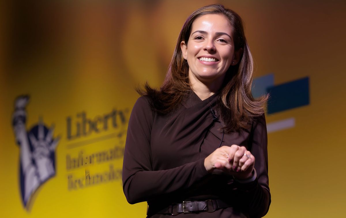 Monica Caldas, global CIO at Liberty Mutual Insurance Company smiling in front of the Liberty Mutual logo.