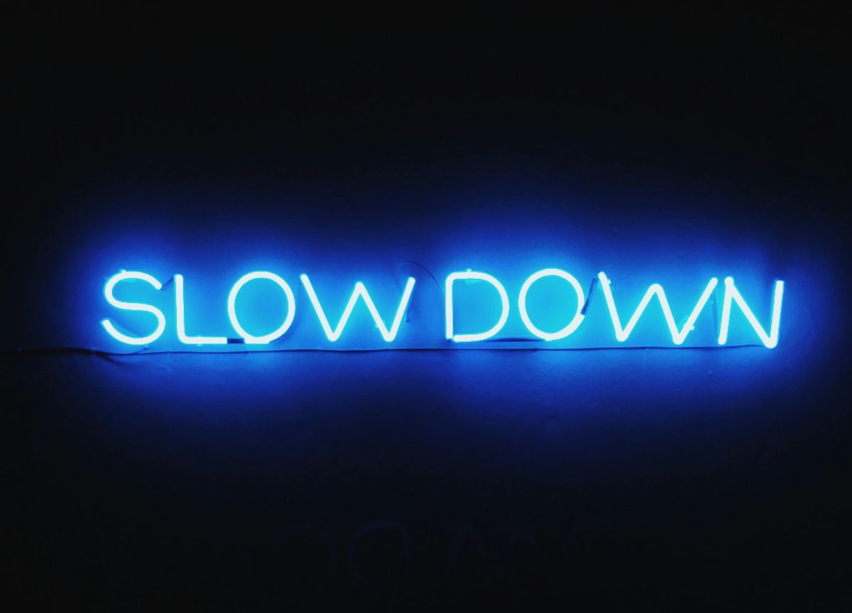 Blue neon sign on a dark background displaying the words “SLOW DOWN.”