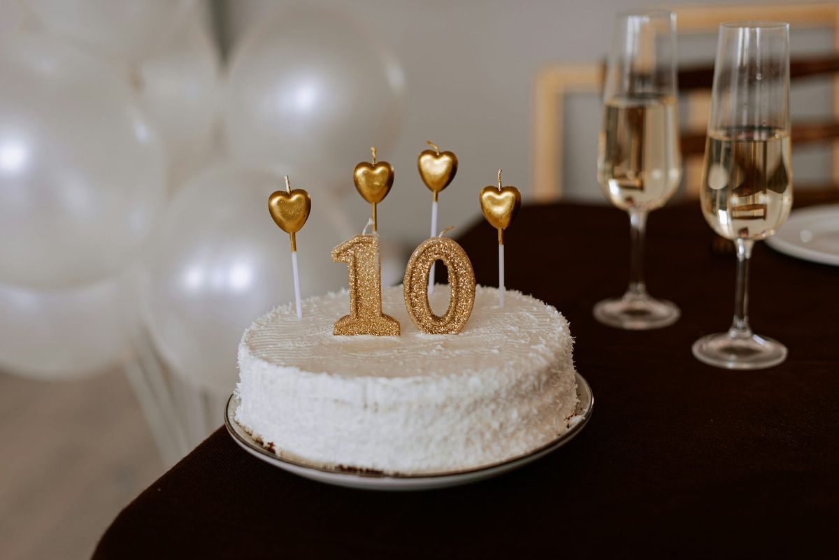 White cake with gold “10” candles, champagne glasses, balloons behind.