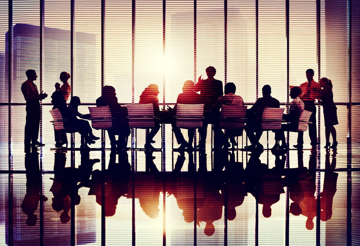 Silhouettes of business people meeting in a glass-walled office at sunset.