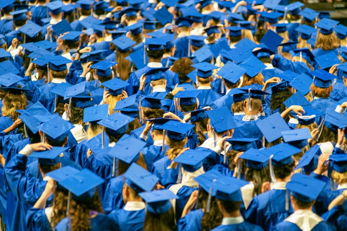 Sea of graduates in blue caps and gowns viewed from behind at a ceremony