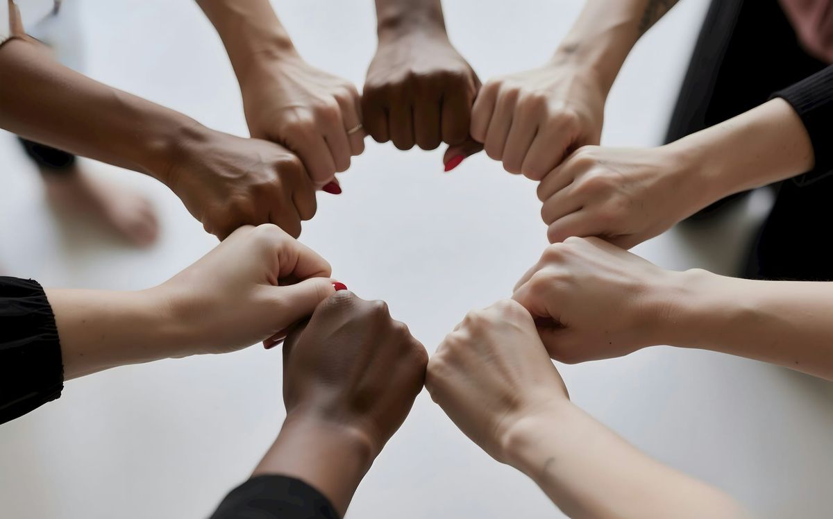Several hands form a circle of fist bumps, shot from below.