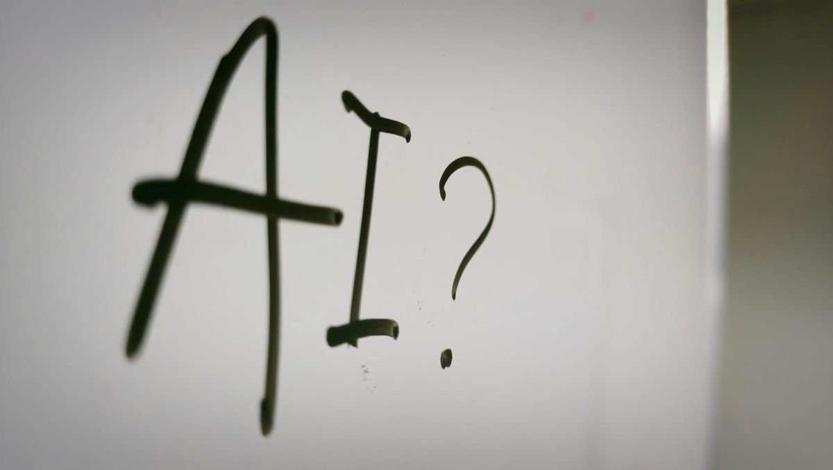 "AI?" written on a whiteboard in dark marker, slightly out of focus.