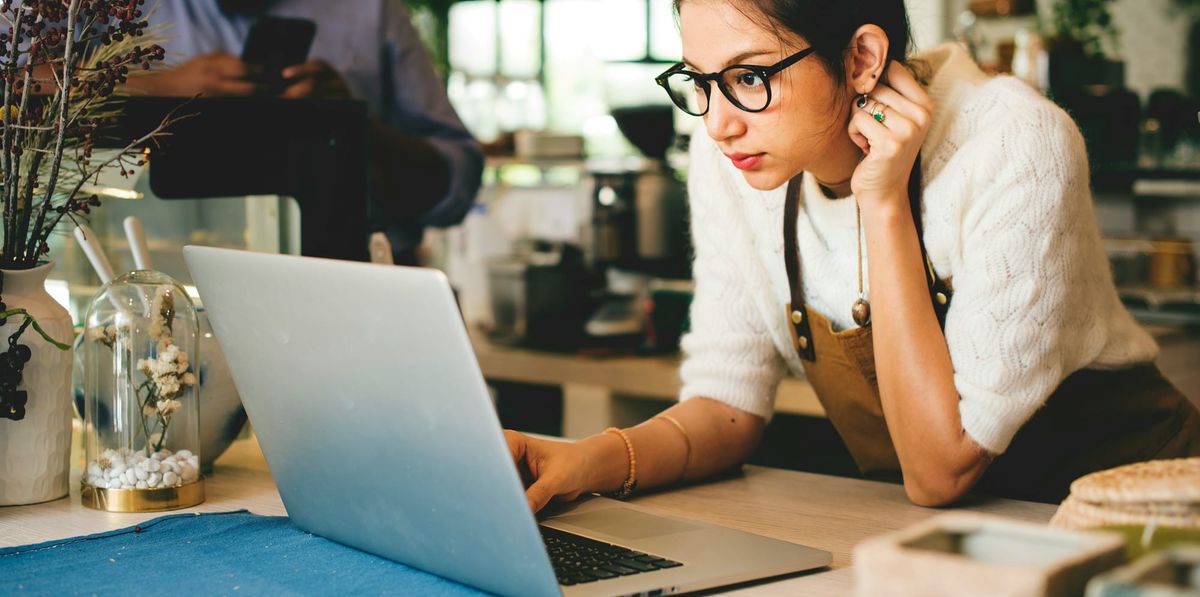 Female small biz owner in shop peering at laptop.