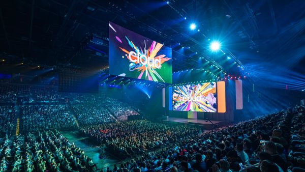 Shot of stadium full of people with two large TVs with Google Cloud on rainbow background above crowd. Taken at Google Cloud