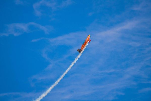 A small red airplane flying through a blue sky