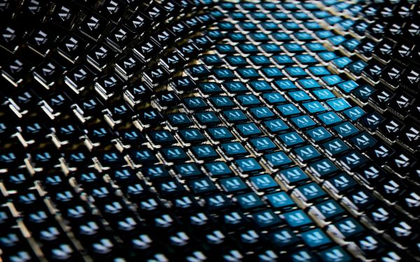 Close-up view of rows of computer chips labeled “AI,” arranged in a grid pattern with alternating blue and black colors, crea